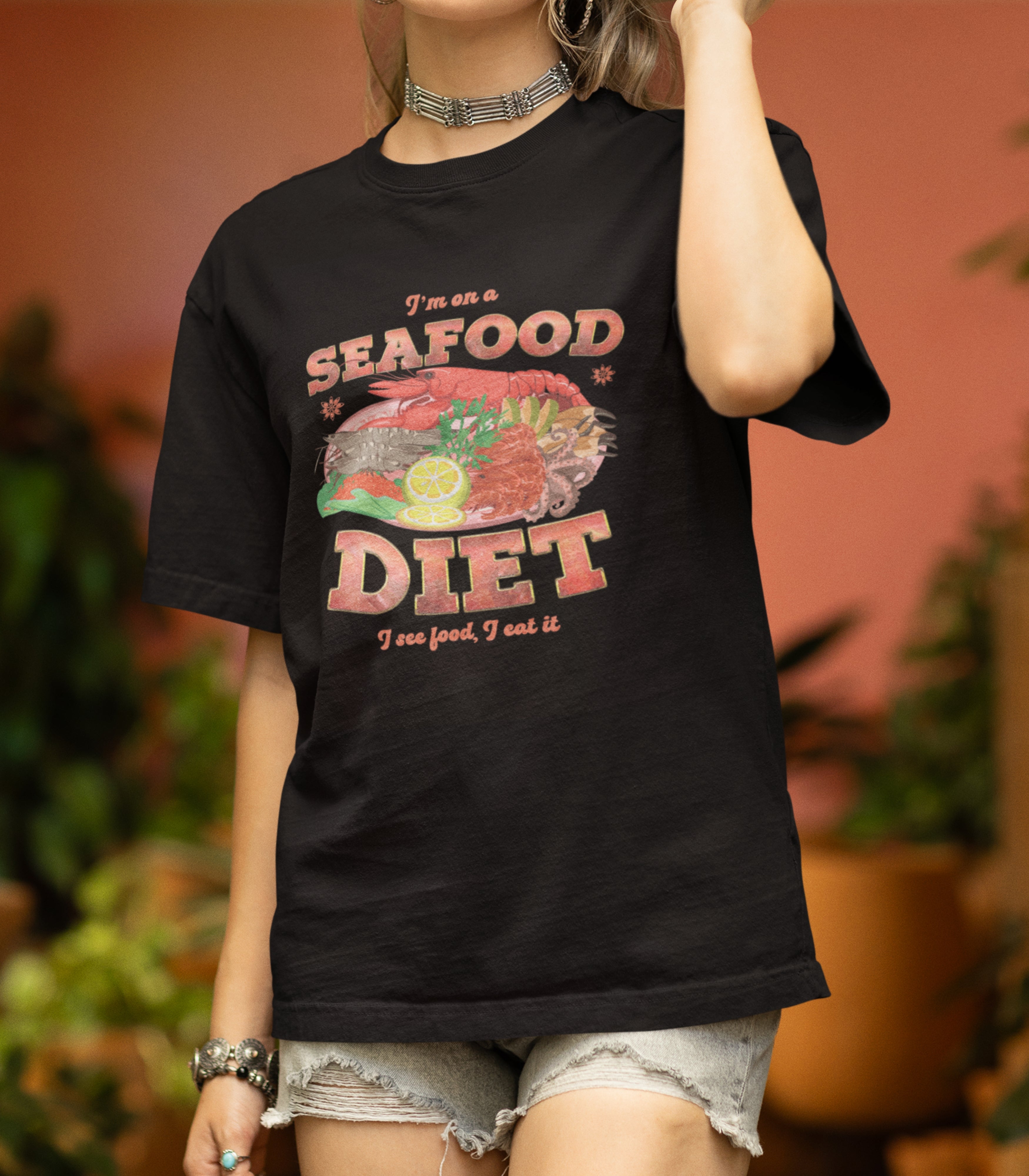 A person wearing a black t-shirt with a graphic print that reads 'I'm a Seafood Diet' and includes images of seafood like lobster, crab, and shrimp.